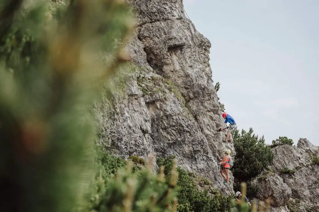three people climbing up a via ferrata on rock face in the alps