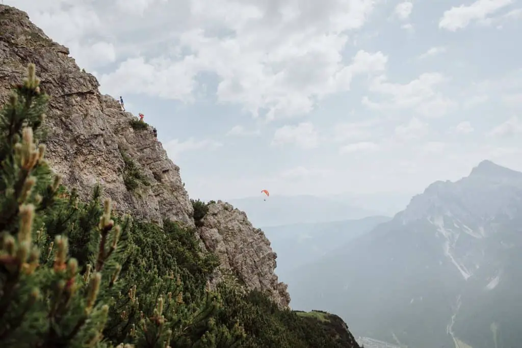 The climbers on a via ferrata in the Austrian Alps with a paraglider in the distance