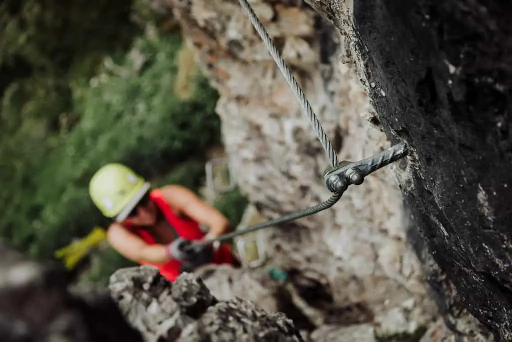 Woman (out of focus) climbing up steel via ferrata cable (in focus)