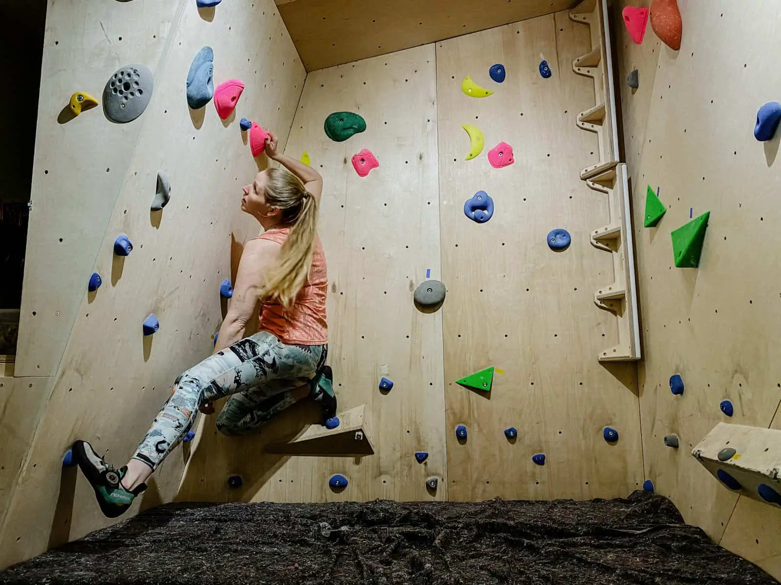 female climbs on indoor bouldering wall in under armour climbing leggings