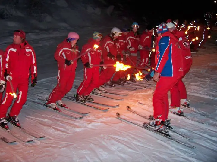 ski instructors line up with torches for a night skiing demonstration