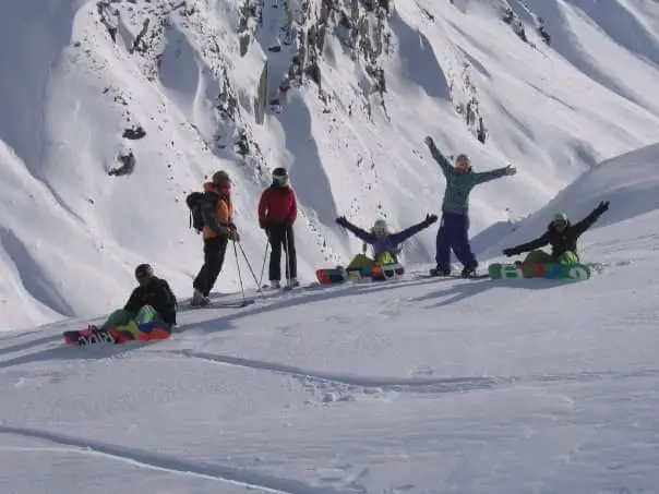 A group of skiers and snowboarders standing and sitting on the side of a mountain in New Zealand during ski instructor training