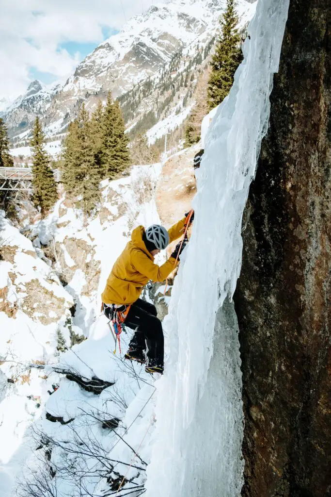 Man in a yellow jacket ice climbing on a frozen water in the Alps