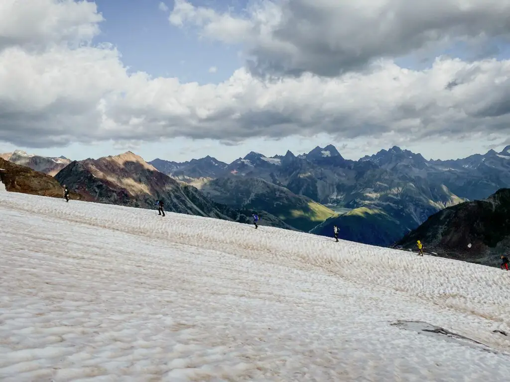 Group of hikers cross a glacier in Tirol. They are roped together and spaced out on the ridge.