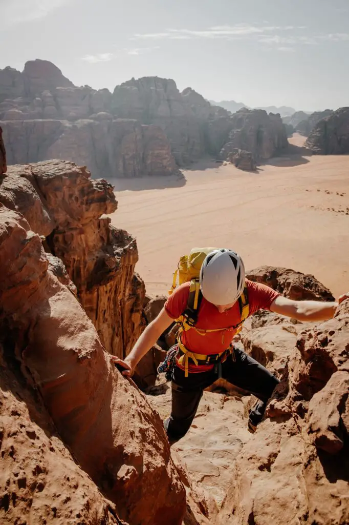 A man in a red t-shirt scrambling in Wadi Rum in Jordan