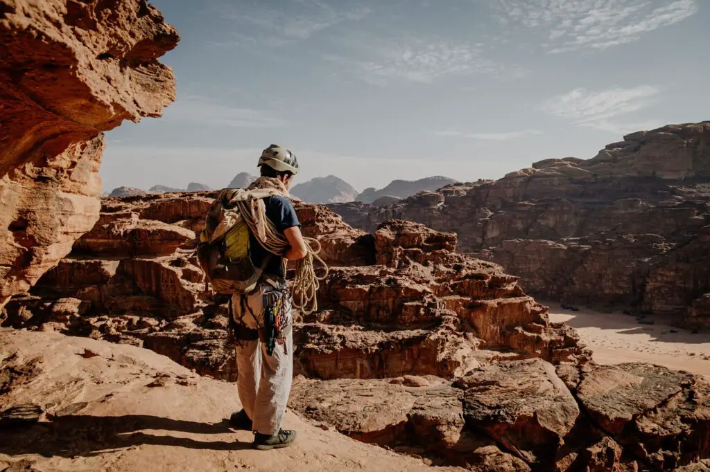 A rock climber standing on the top of a mountain with his rope over his shoulders, looking at the view over Wadi Rum in Jordan